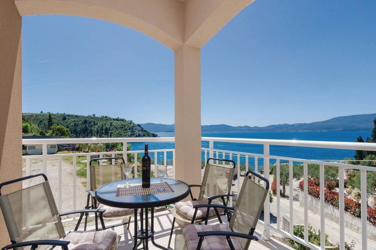 A balcony with a round table and chairs, overlooking a scenic view of the sea and mountains.