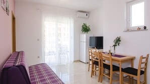 A compact living space with a kitchenette, a dining area with a table and chairs, a sofa, and a TV. - Apartments Ljuba (Slivno)