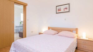 A bedroom with a bed, bedside tables, a nightstand, a wooden wardrobe, and a framed picture on the wall. - Apartments Ljuba (Slivno)
