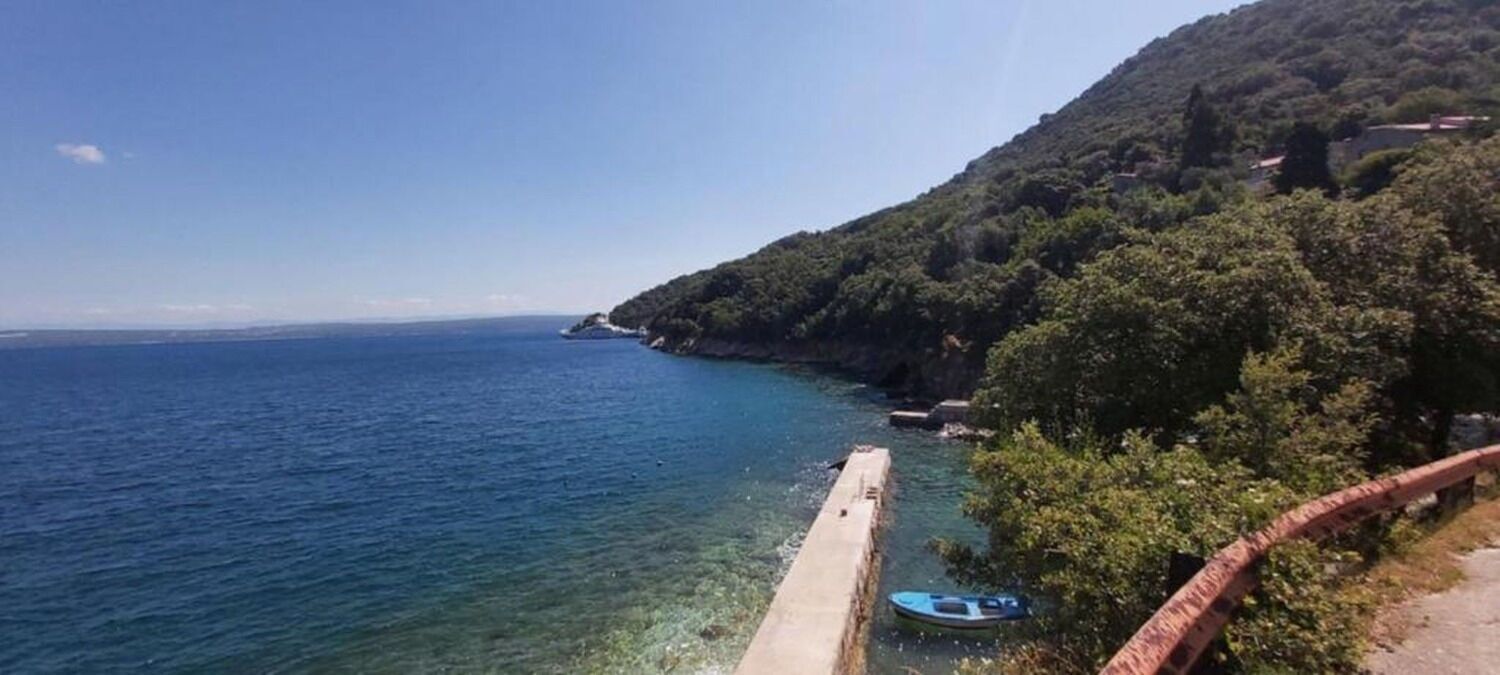 Ένα παράκτιο τοπίο με καθαρή θέα στη θάλασσα, μια προβλήτα από σκυρόδεμα και ένα σκάφος.