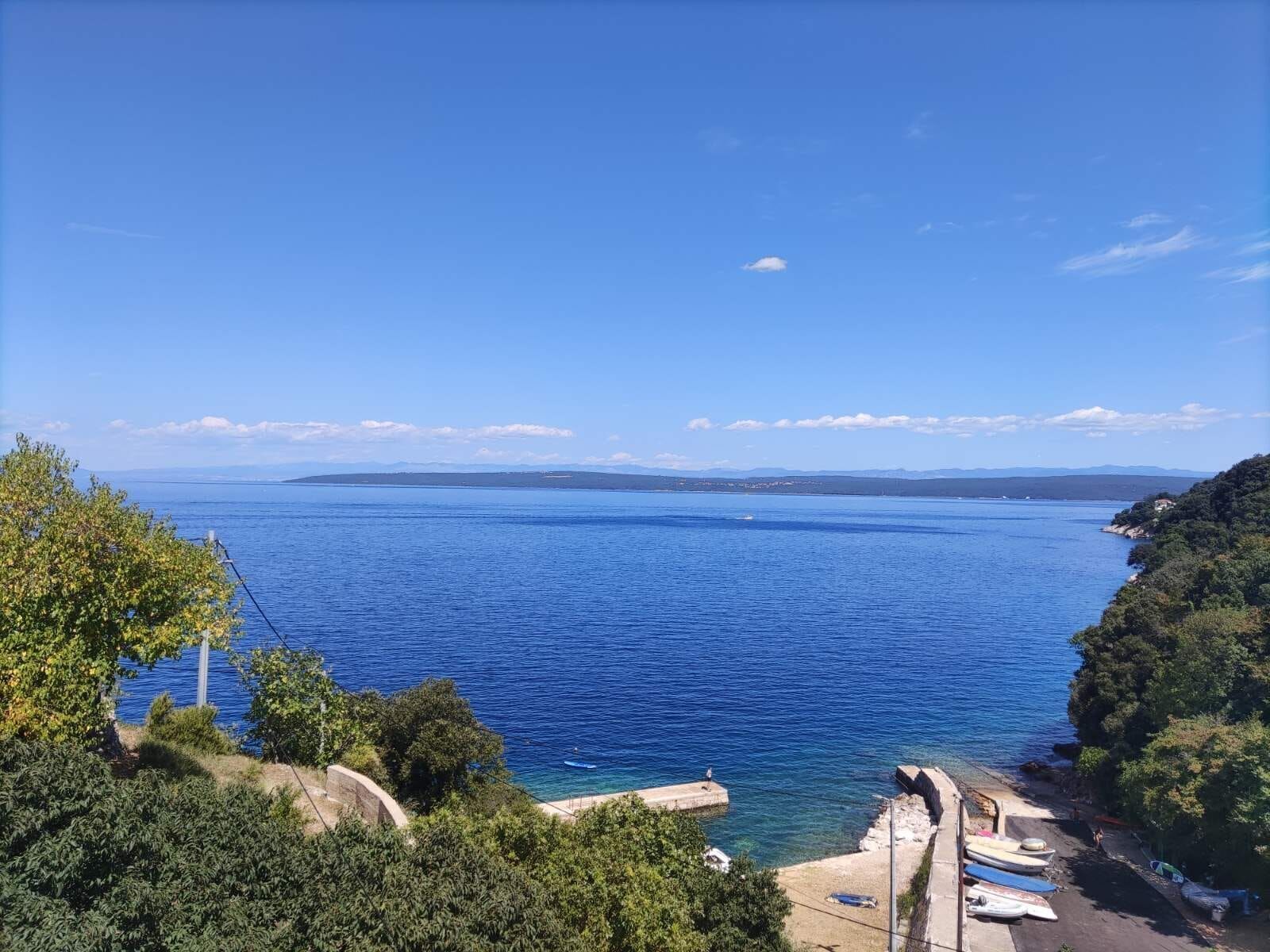 A coastal view with a clear blue sea, a rocky shoreline, and a small pier with boats.