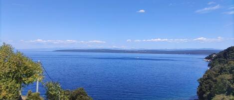 A coastal view with a clear blue sea, a rocky shoreline, and a small pier with boats.