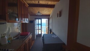 Een smalle keuken met houten kastjes, een spoelbak en een raam dat uitkomt op een balkon.