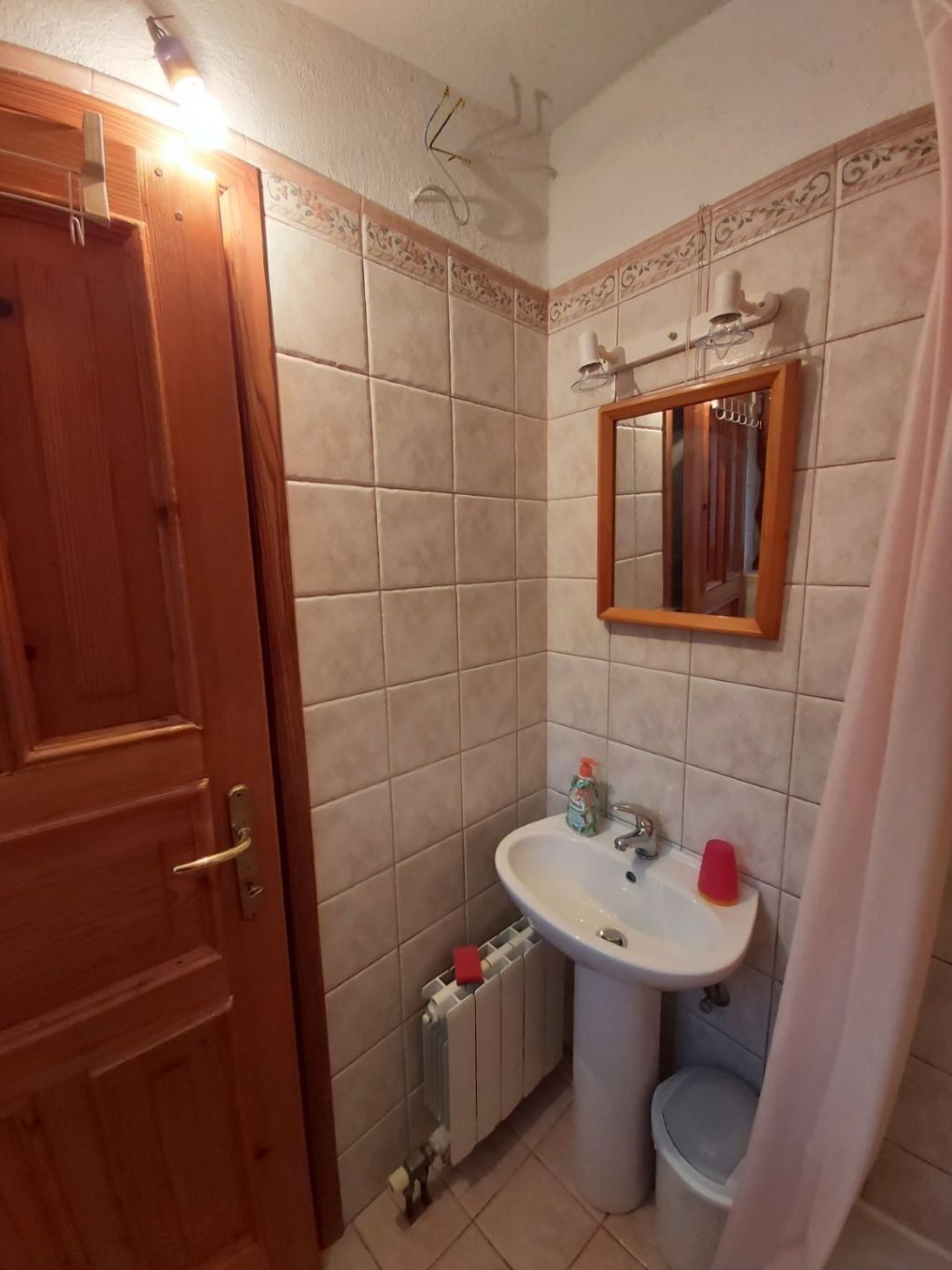 Une salle de bain avec une porte en bois, un lavabo blanc, un miroir et des toilettes.