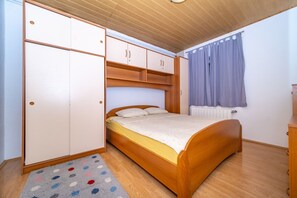 A bedroom with a wooden bed, a wardrobe, and a window with curtains. - Apartment Zoran (Postira)