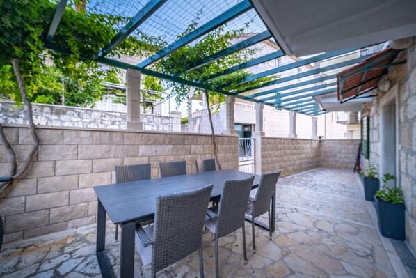 An outdoor patio with a table and chairs, a stone floor, and a pergola structure. - Apartment Zoran (Postira)