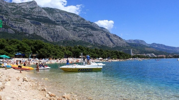 A beach with clear water, a boat named 'PARASAIL', and mountains in the background. - Apartment Anytime (Makarska)