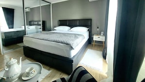 Ett modernt hotellrum med en stor säng, ett nattduksbord med en lampa, en spegel och ett bricka med en tekanna och en kopp.