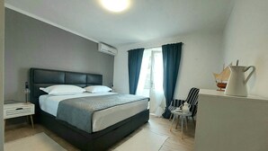 A modern hotel room with a large bed, a small table with a ship-shaped lamp, and a chair. - Apartment Anytime (Makarska)