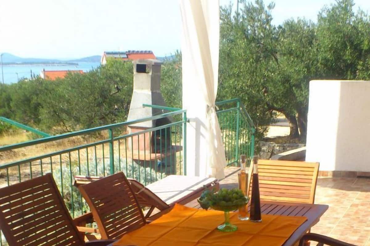 Una terrazza esterna con tavolo e sedie, una tenda bianca e vista sul mare e sugli edifici sullo sfondo.