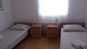 A small, clean room with two single beds, wooden nightstands, and a window with a curtain. - Apartments Dia (Primosten)