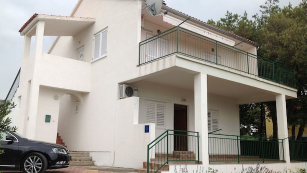 A two-story building with a balcony, a satellite dish, and a car parked in front. - Apartments Dia (Primosten)