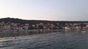 A coastal town with buildings along the waterfront, boats docked, and a hilly landscape in the background. - Apartment Tome (Tisno)