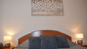 A neatly made bed with a wooden headboard, two bedside lamps, and a wall-mounted painting above it. - Apartment Tome (Tisno)