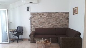 A living room with a brown sofa, a small coffee table, a black office chair, and a stone-patterned wall. - Apartment Tome (Tisno)