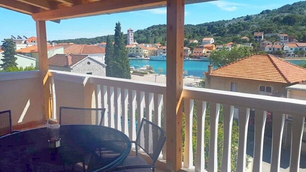 A balcony with a table and chairs, overlooking a coastal town with buildings and a clear view of the sea. - Apartment Tome (Tisno)