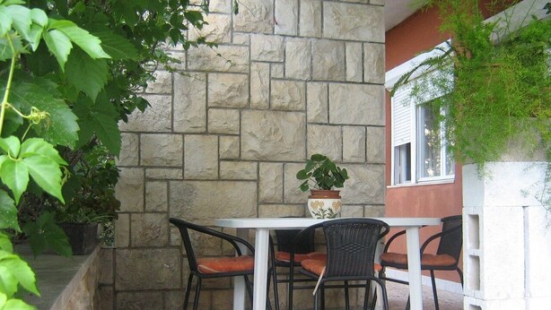 An outdoor patio with a stone wall, a round table, and four chairs. - Apartment Dane (Makarska)