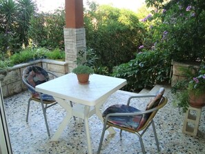An outdoor patio with a white table and two chairs, surrounded by lush greenery and potted plants. - Apartment Dane (Makarska)