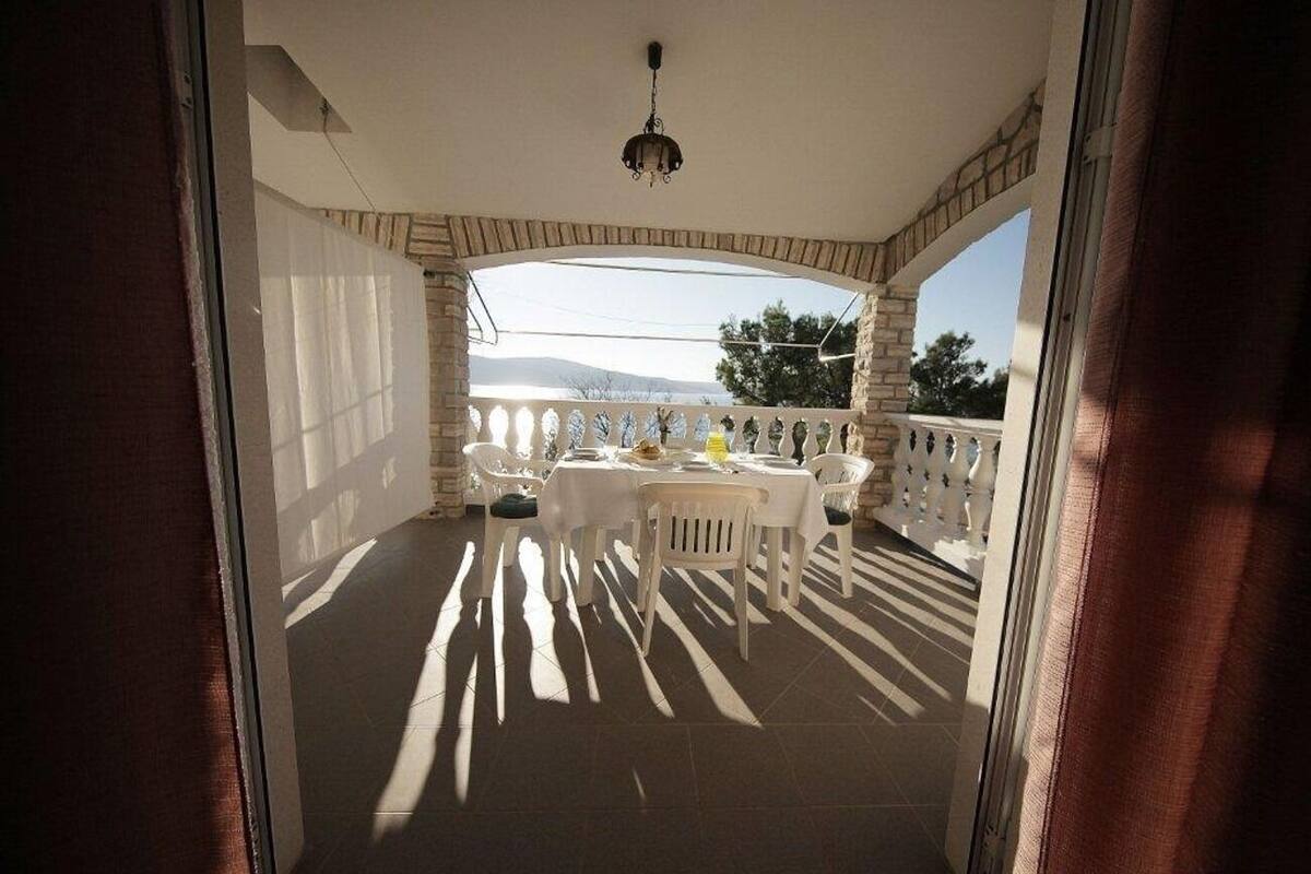 A covered outdoor dining area with a table and chairs, a view of the landscape, and a ceiling light.