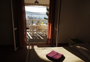 A room with a bed, a small table with a chair, and a view of a balcony with a table and chairs outside. - Apartments Ivan Z (Starigrad)