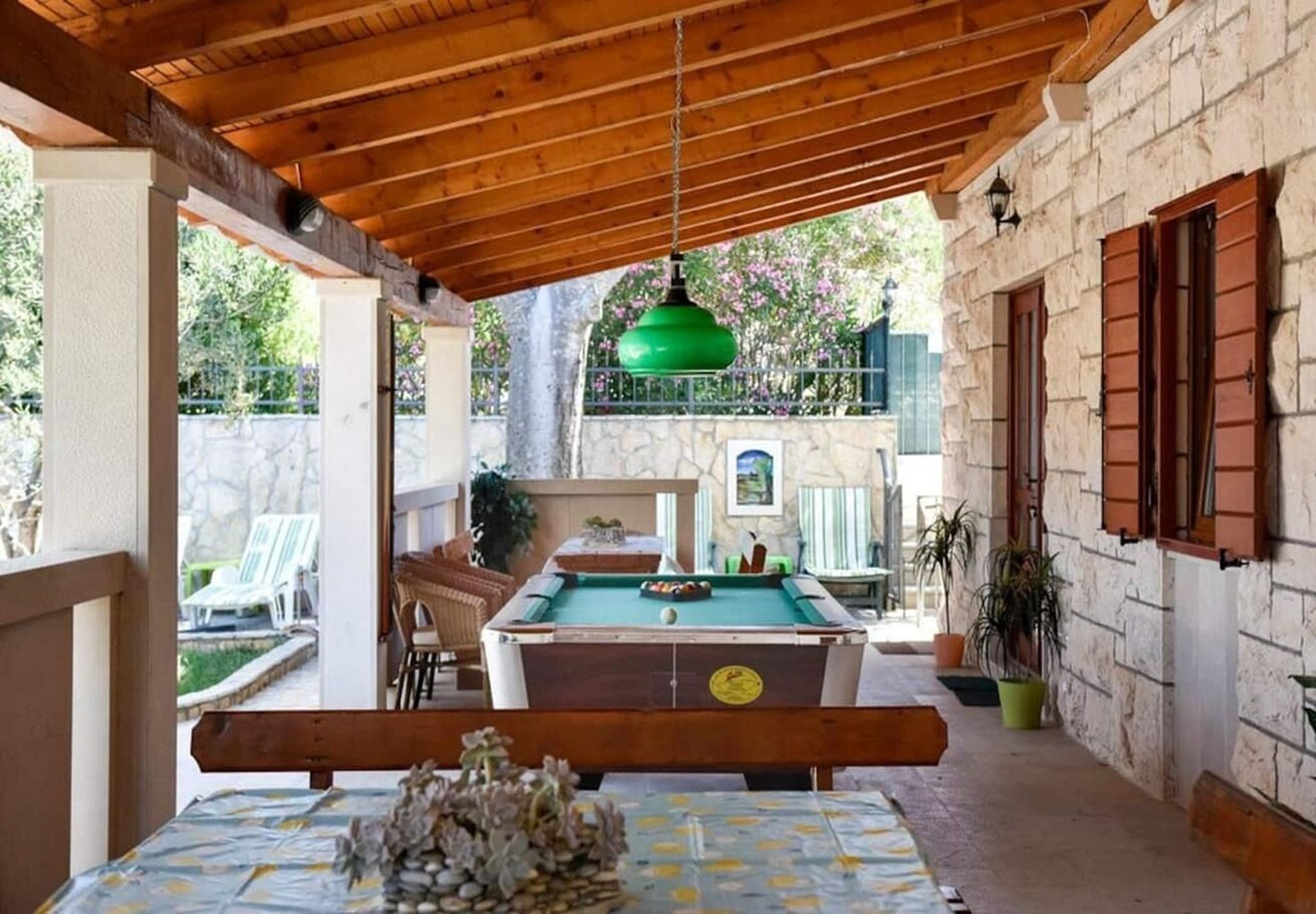Un espacio al aire libre cubierto con mesa de billar, asientos y un edificio de piedra al fondo.