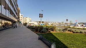 A modern building with a glass facade, a landscaped area with grass and shrubs, and a clear view of the sea in the background. - Apartment Deni (Split)