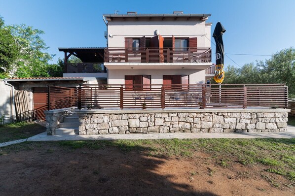 Une maison à deux étages avec des fondations en pierre, un balcon et une cour avant clôturée.