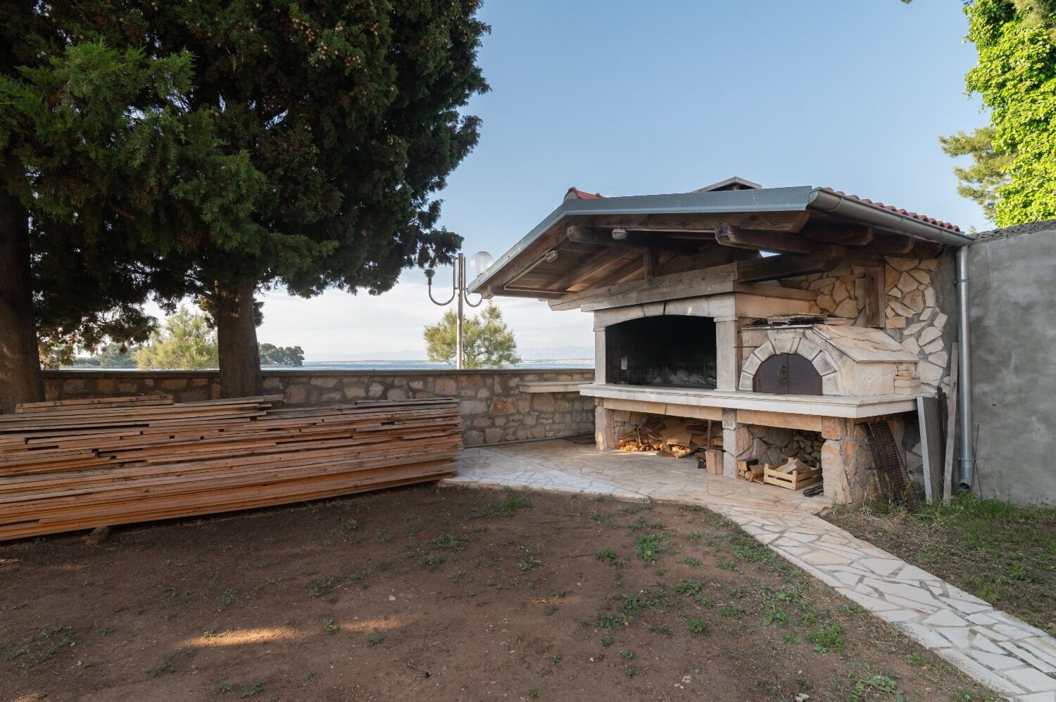 Una chimenea de piedra al aire libre con una chimada, rodeada por un muro de piedra y un banco de madera.