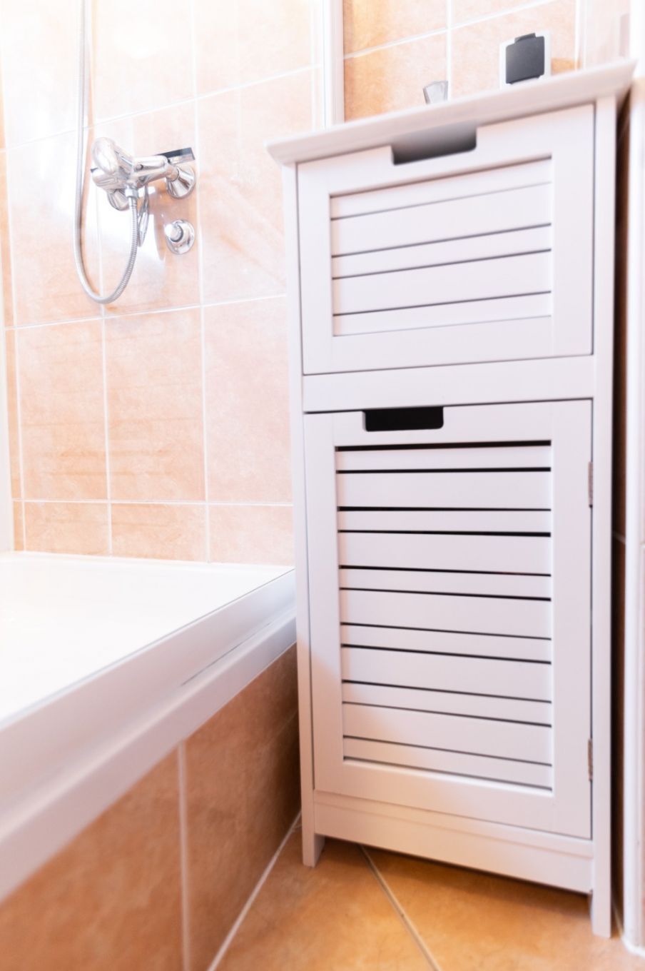 A bathroom with a white bathtub, a showerhead, and a cabinet with horizontal lines.
