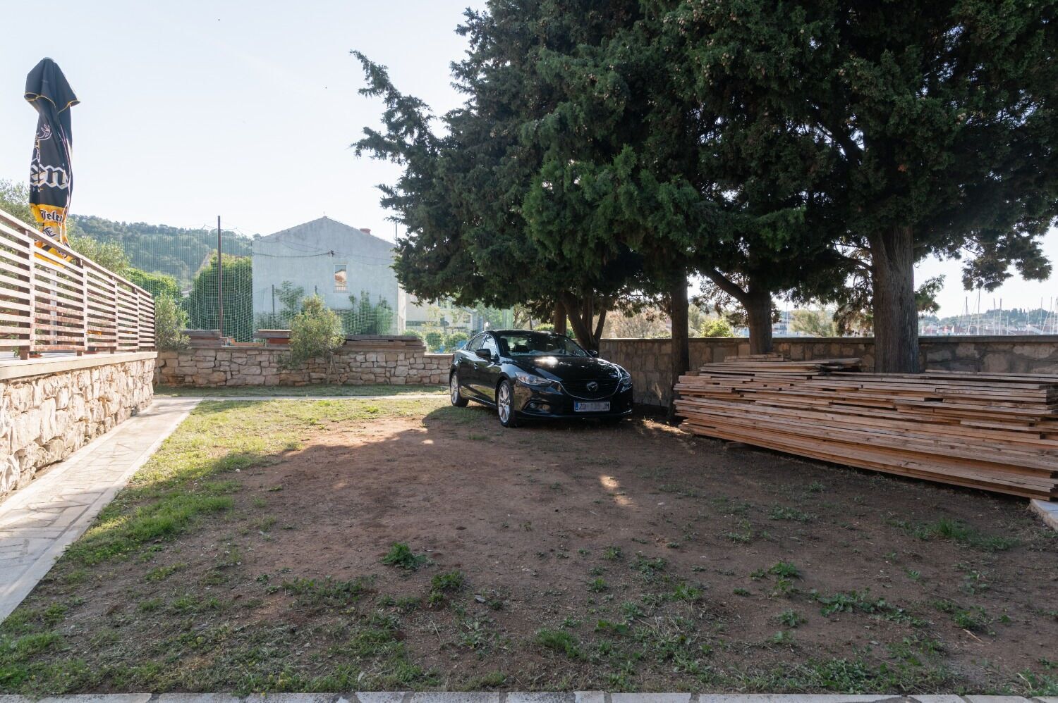 A car parked in a dirt area with a stone wall and a wooden fence.