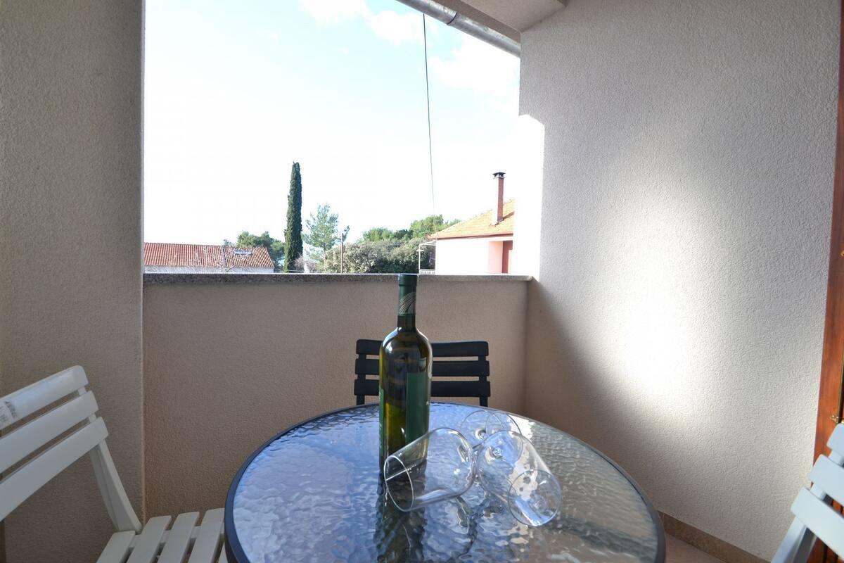 Un petit balcon avec une table ronde en verre, une bouteille de vin et deux verres à vin vides.