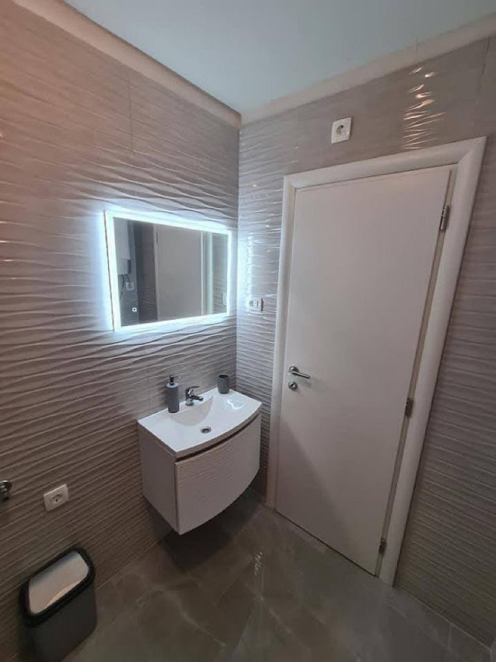 A modern bathroom with a vanity, a mirror, and a door.