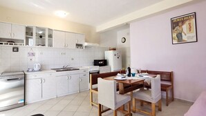 A compact kitchen with white cabinets, a dining table set for four, and a refrigerator. - Apartments Vinx (Rogoznica)