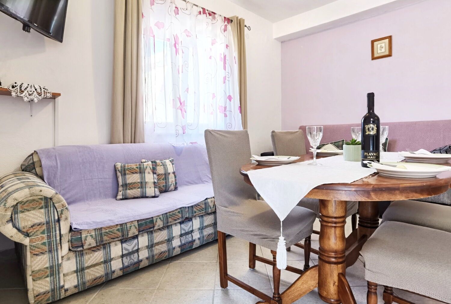 Un área de comedor con una mesa de madera, un sofá y un televisor montado en la pared.