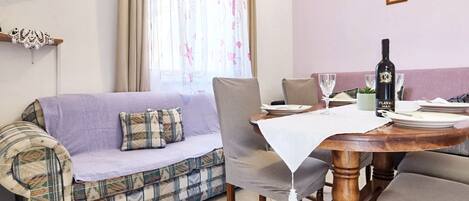 Un área de comedor con una mesa de madera, un sofá y un televisor montado en la pared.