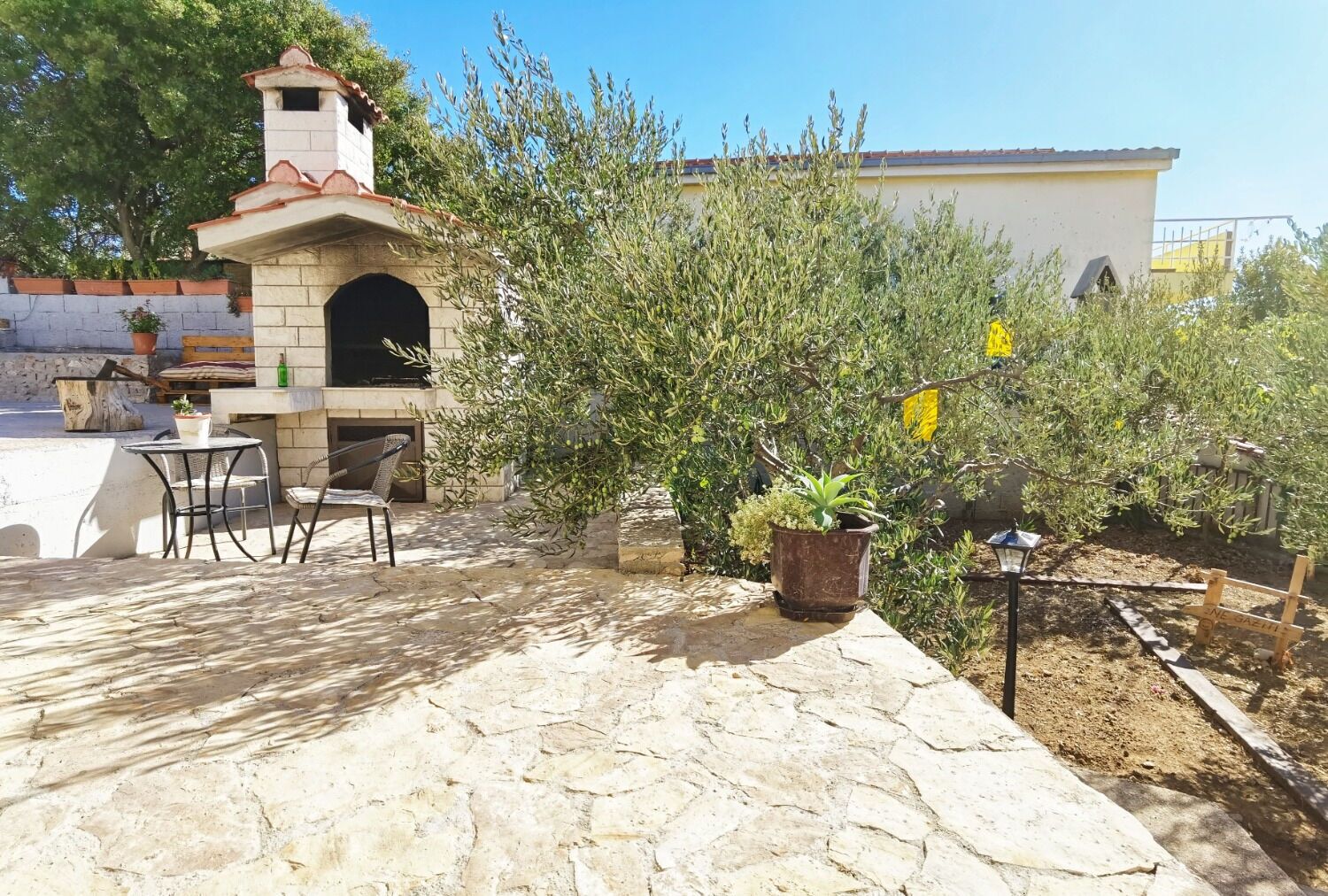 Un patio con suelo de piedra, una parrilla de ladrillo, mobiliario de exterior y plantas en macetas.