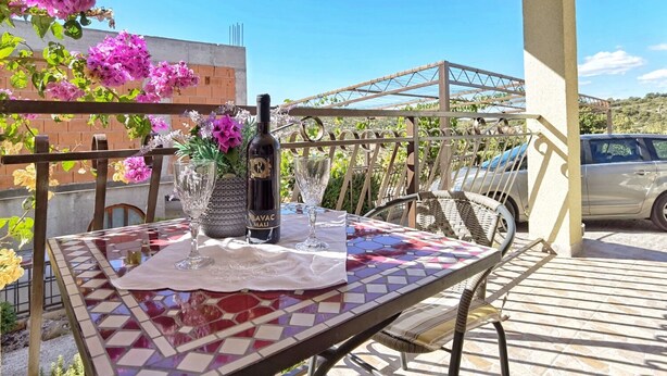 A patio with a table set for two, a bottle of wine, and a vase with flowers. - Apartments Vinx (Rogoznica)