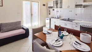 A modern kitchen with white cabinets, a dining table set for two, and a sofa in the living area. - Apartments Vinx (Rogoznica)
