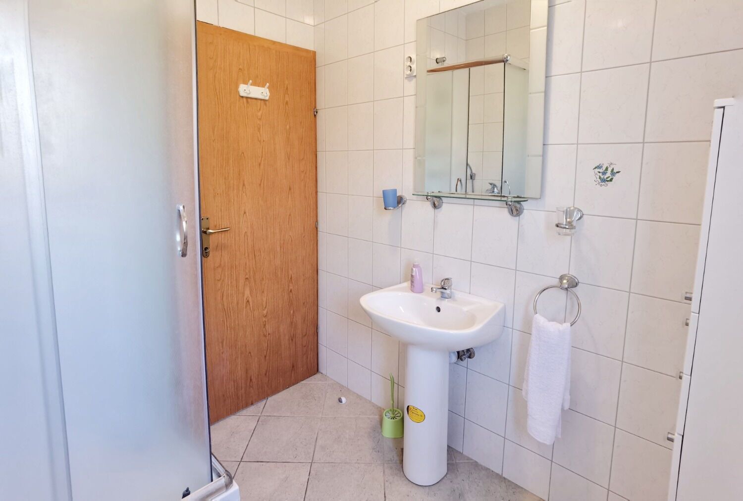 A bathroom with a wooden door, a white sink, a mirror, and a towel rack.