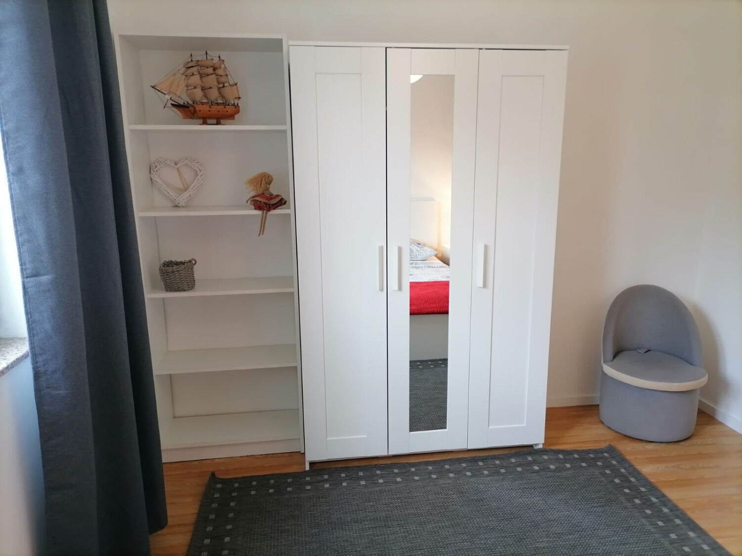 Ett rum med en vit garderob, en grå stol och en liten modell av ett skepp på den översta hyllan.