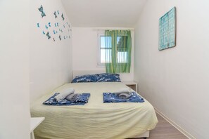 Ein Schlafzimmer mit Bett, Kissen, einem Fenster mit Vorhängen und Wanddekorationen.