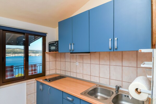 A kitchen with blue cabinets, a wooden countertop, a stainless steel sink, and a view of the sea. - Apartment Denis (Okrug)