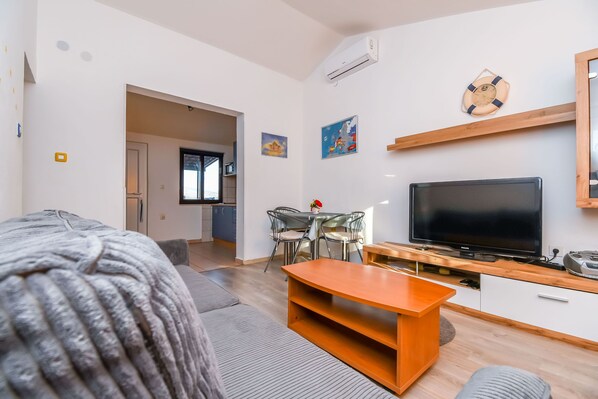 Ein modernes Wohnzimmer mit Sofa, Couchtisch, Fernseher und Essbereich.