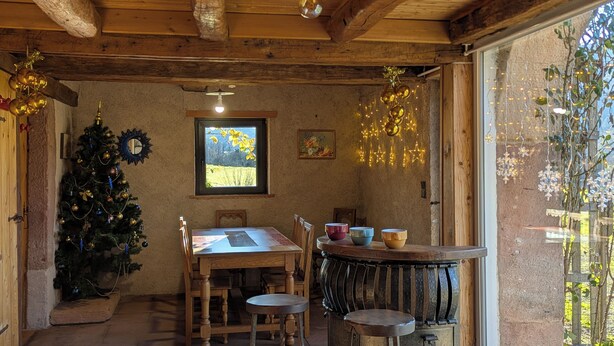 A rustic dining area with a wooden table and chairs, a Christmas tree, and a window with a view of a field. - La Mignonne, Vosges mountains, private spa 8 people near Gérardmer (Laveline-du-Houx)