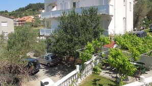 Un immeuble résidentiel à plusieurs étages, doté de balcons, entouré de verdure et bordé de voitures garées.