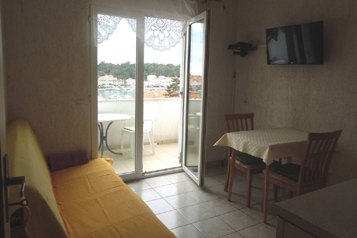 A room with a bed, a table, and chairs, a TV mounted on the wall, and a sliding glass door leading to an outdoor area.