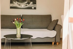 A living room with a grey sofa, a round coffee table with a vase of tulips, and a painting on the wall.