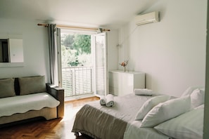 Un dormitorio con cama, sofá, mesita de noche y ventana con vistas a zonas verdes.