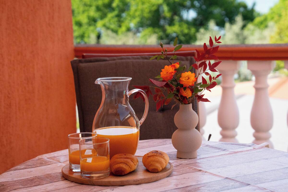 Ein Frühstücksangebot mit einem Orangensaftkännchen, zwei Gläsern und zwei Croissants auf einem Holftablett.