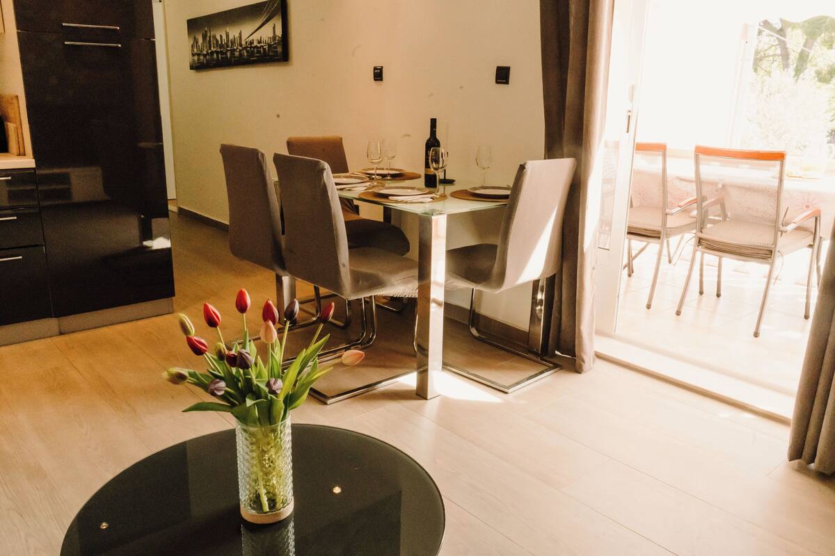 Ein Essbereich mit einem Tisch für zwei Personen, einer Vase mit Tulpen und einem Stadtbild an der Wand.